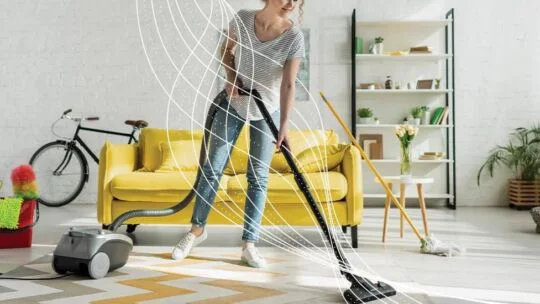 Person, die einen modernen Staubsauger auf einem Teppich in einem hellen Raum verwendet