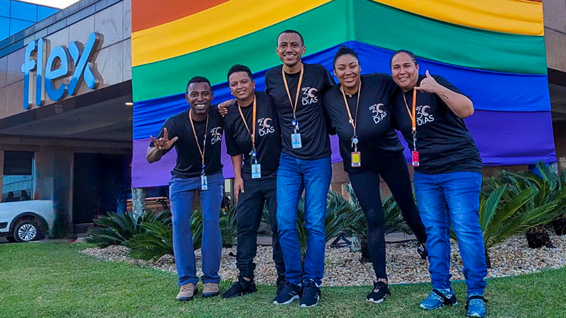Empleados de Flex en Brasil parados frente a una bandera del orgullo afuera del edificio Flex